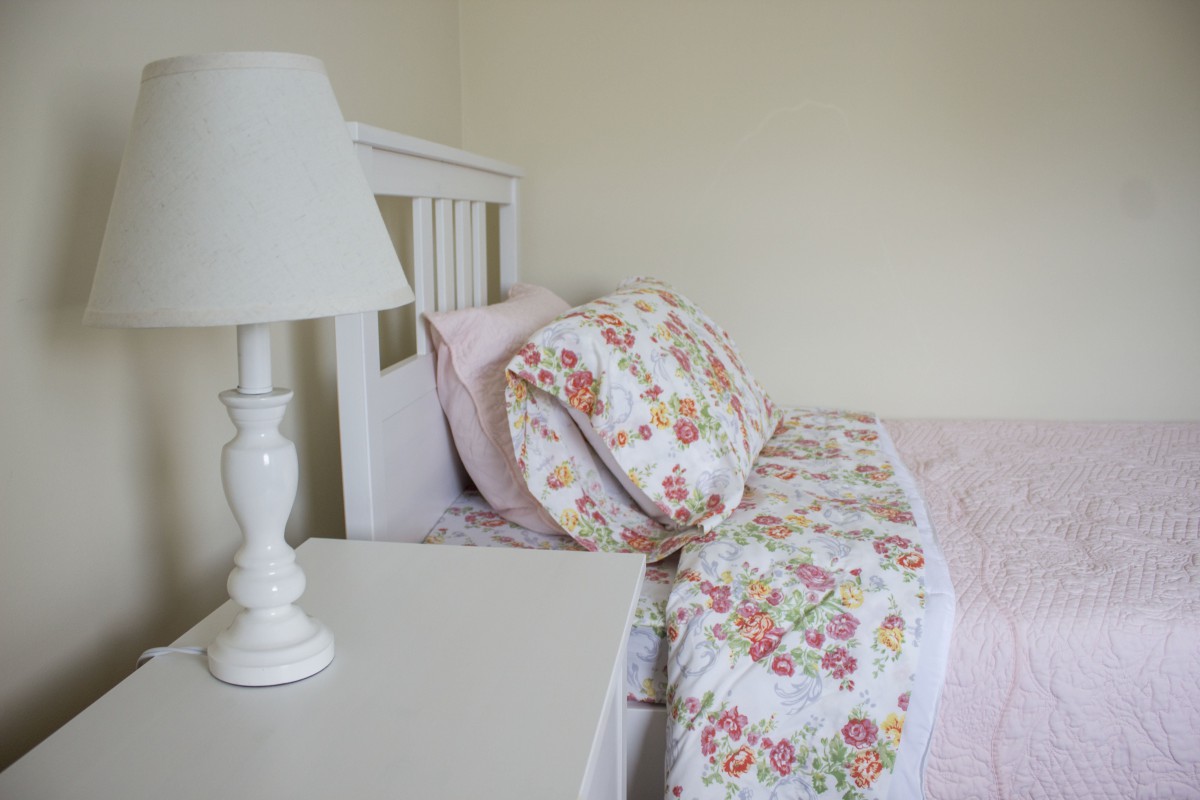 A cozy bedroom setup with floral bedding and a white lamp on the nightstand.