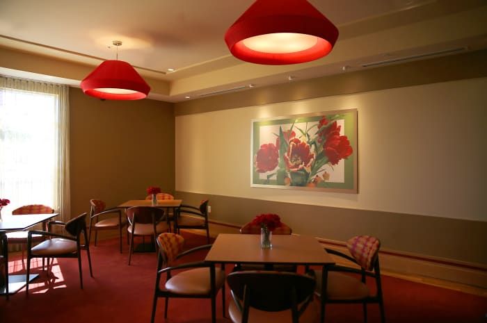 A cozy restaurant interior featuring red lighting, artwork on the wall, and neatly arranged tables and chairs.