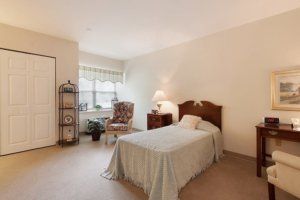 A cozy bedroom featuring a single bed, an armchair by the window, and a soft carpeted floor.