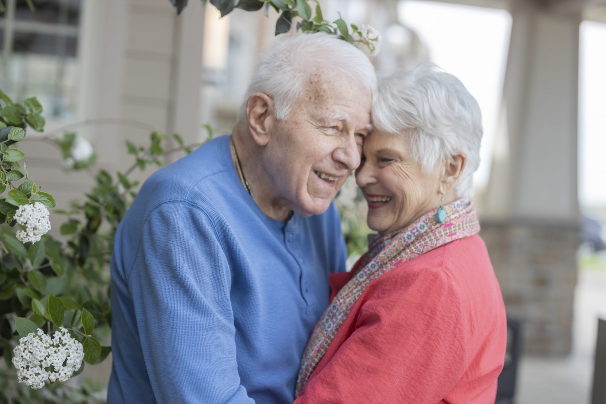 An elderly couple sharing a joyful embrace outside.