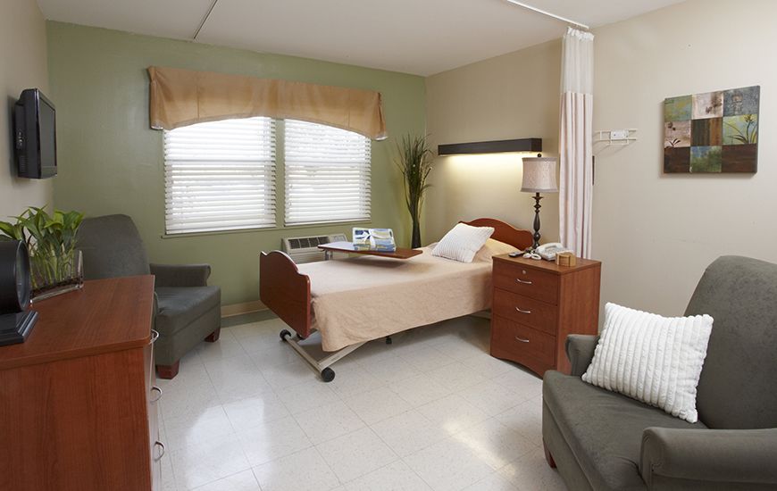 A tidy and well-lit hospital room featuring a bed, side table, and seating area.