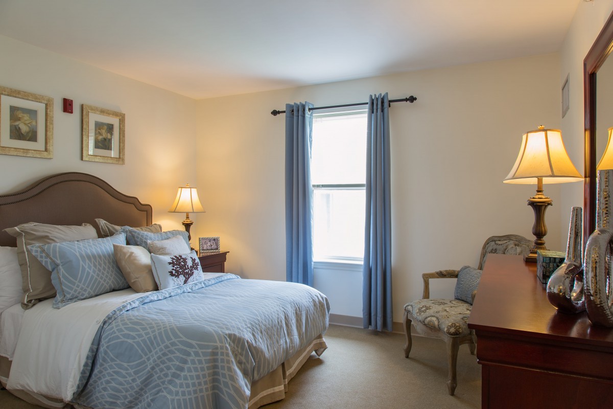 A cozy bedroom with a neatly made bed, soft lighting, and blue curtains.