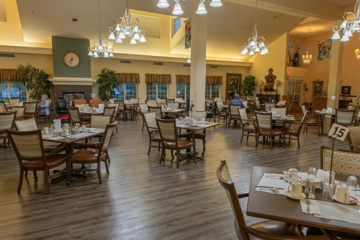 An elegant dining area with neatly arranged tables and chairs, illuminated by chandeliers.