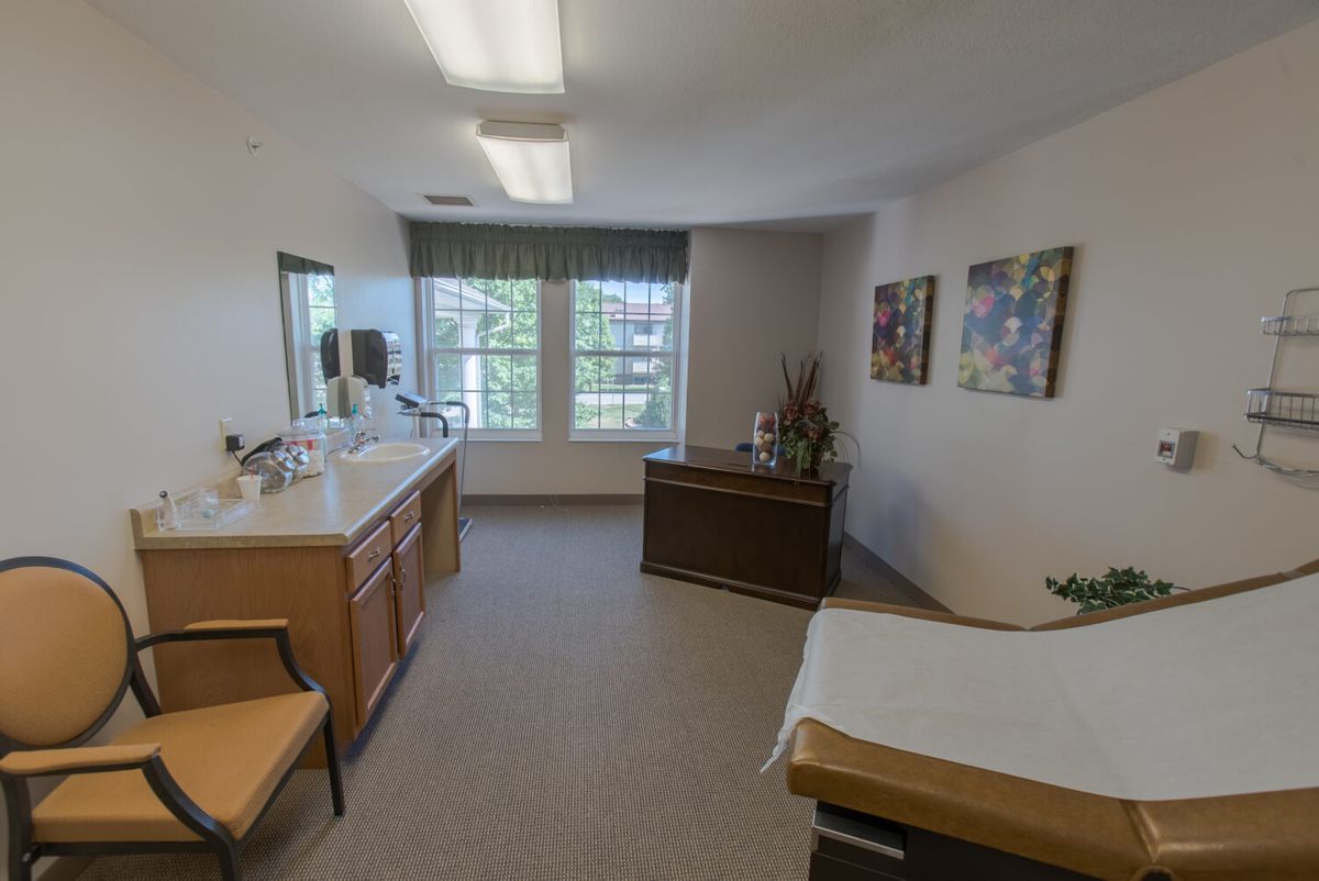 A clean and well-organized medical exam room with a patient bed and a sink area.