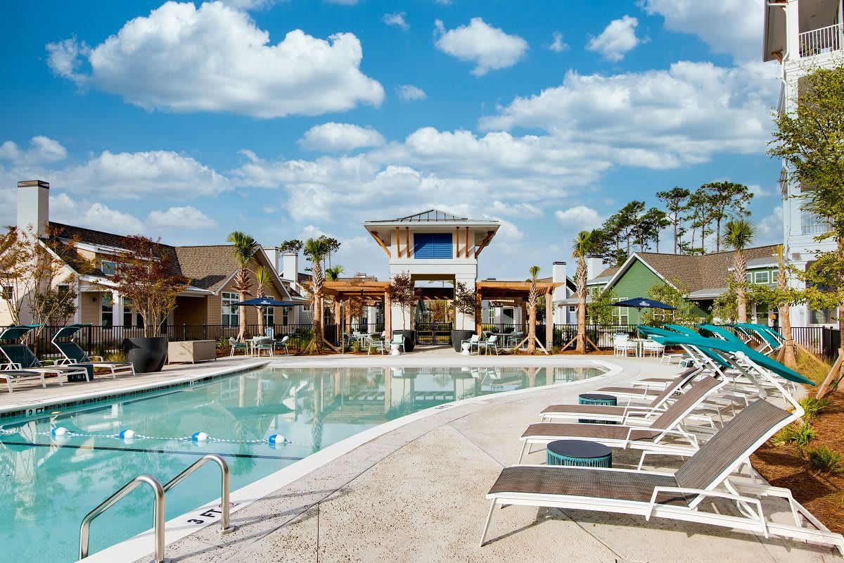A luxurious resort pool with lounge chairs under a bright, blue sky.