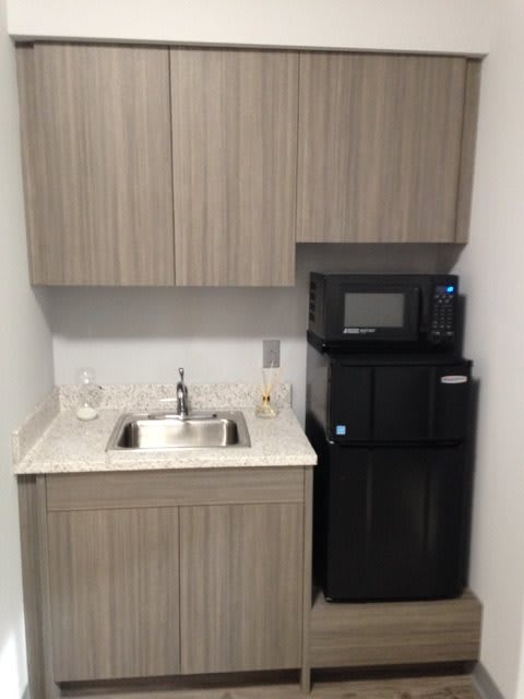Small kitchenette setup with sink, cabinets, microwave, and a water dispenser.