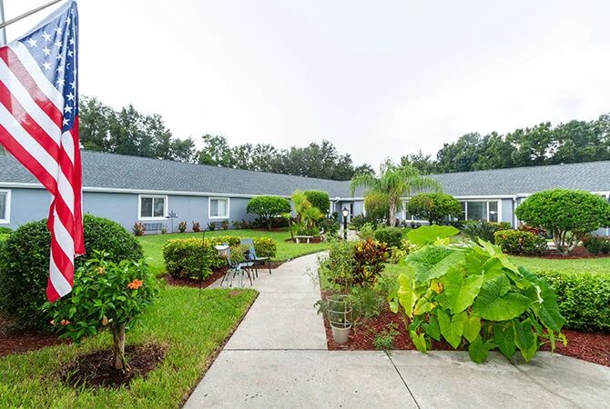 A picturesque garden walkway surrounded by lush greenery and shrubs, leading to a series of connected buildings.
