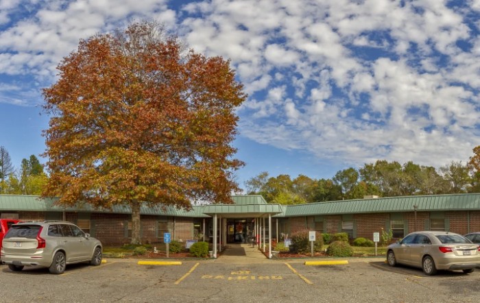 A building with an entrance, surrounded by autumn trees and a cloudy sky.