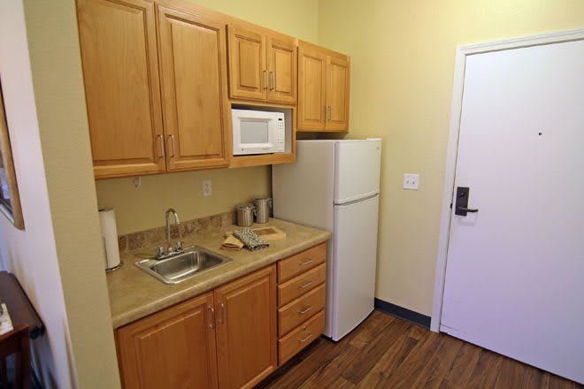 A compact kitchen space with wooden cabinets, a microwave, sink, and refrigerator.
