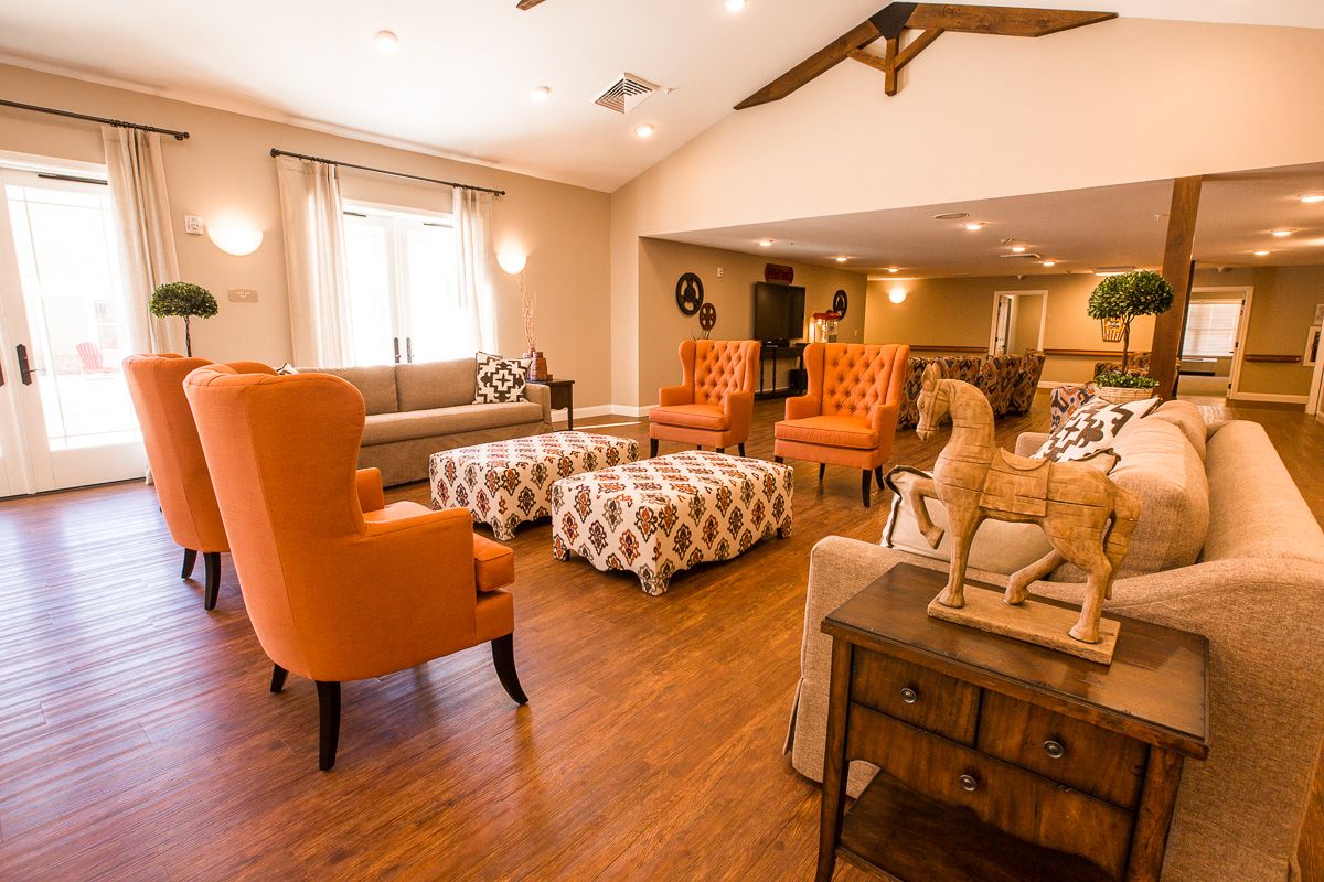 A cozy and brightly lit living room featuring orange chairs and patterned ottomans on a wooden floor.
