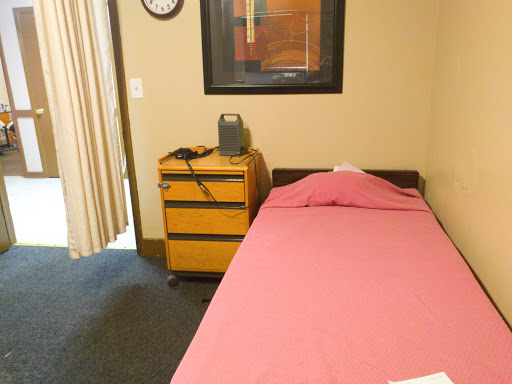 A simple bedroom setup featuring a single bed with pink bedding, a nightstand, and wall art.