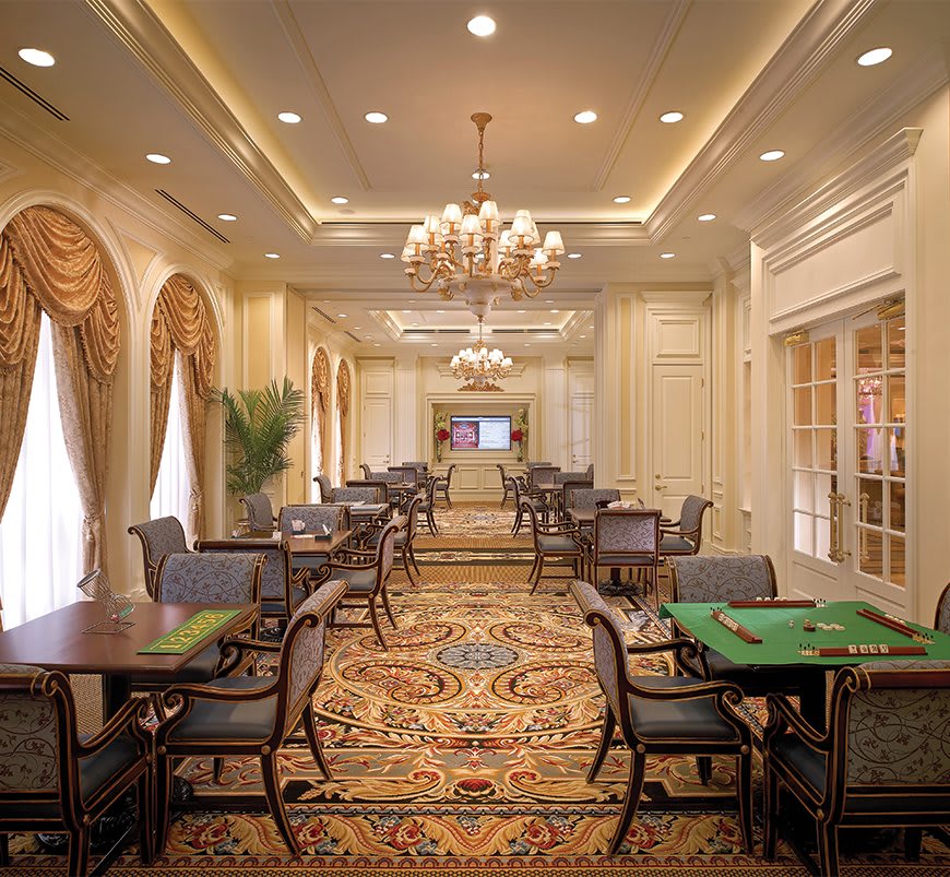 A luxurious dining area with chandeliers, carpeted floors, and elegantly arranged tables and chairs.