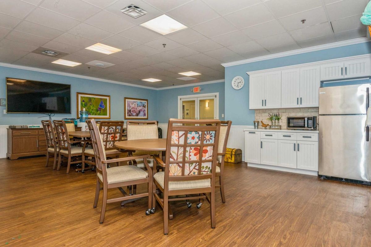 A cozy dining area with wooden tables and chairs, featuring a kitchenette in the background.