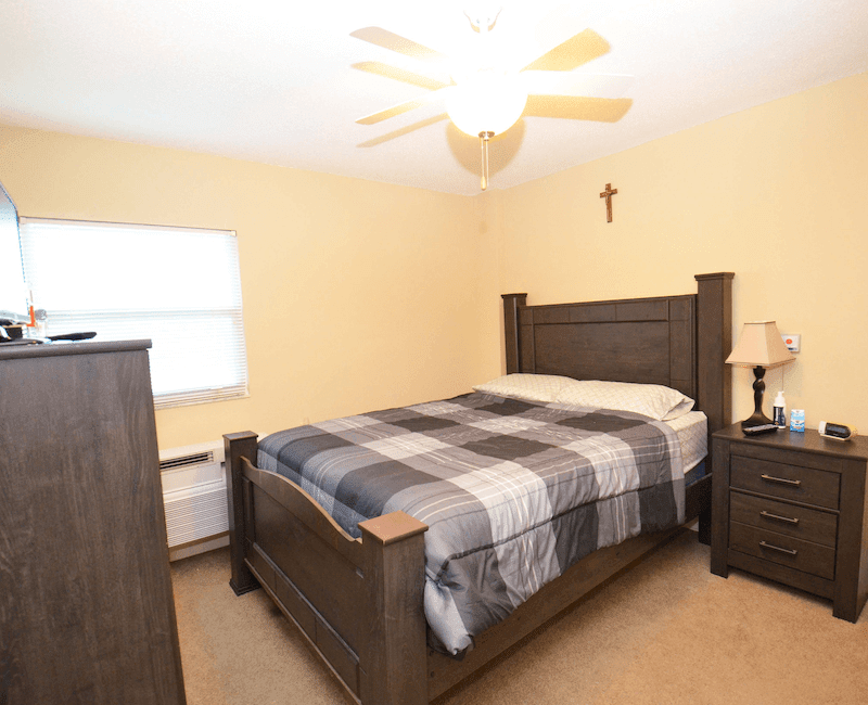 A cozy bedroom with a wooden bed, plaid blanket, and warm lighting.