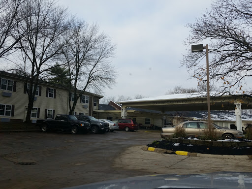 A view of a parking area with several cars parked near two buildings under a cloudy sky.