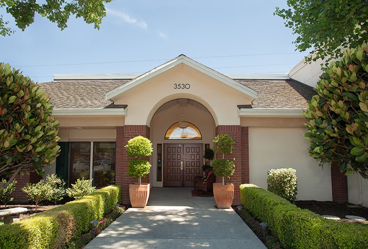 A front view of a building entrance with potted plants and neatly trimmed bushes.