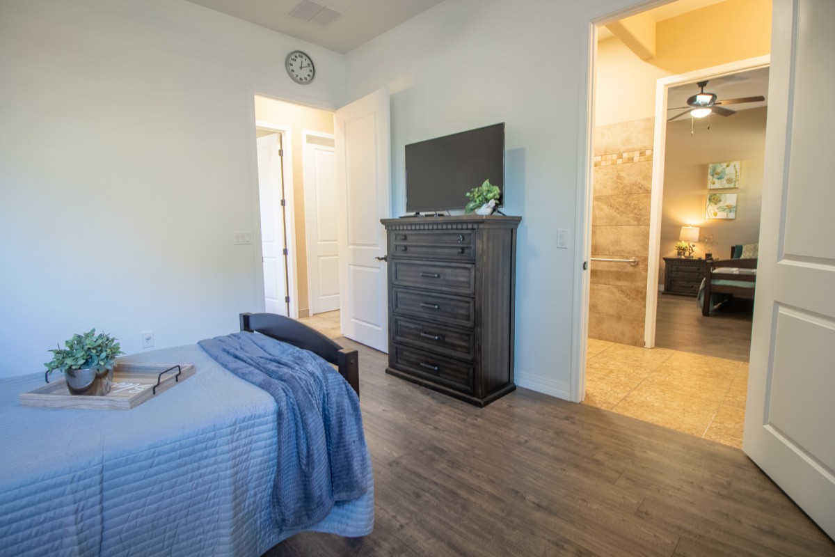 A cozy bedroom interior featuring a bed, chest of drawers with a television, and an open door to an adjoining room.