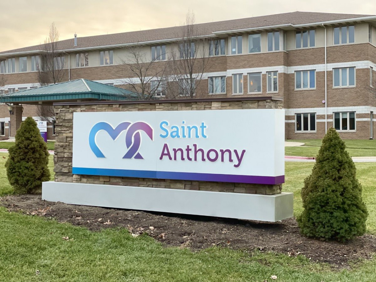 A sign for Saint Anthony hospital stands in front of a brick building.