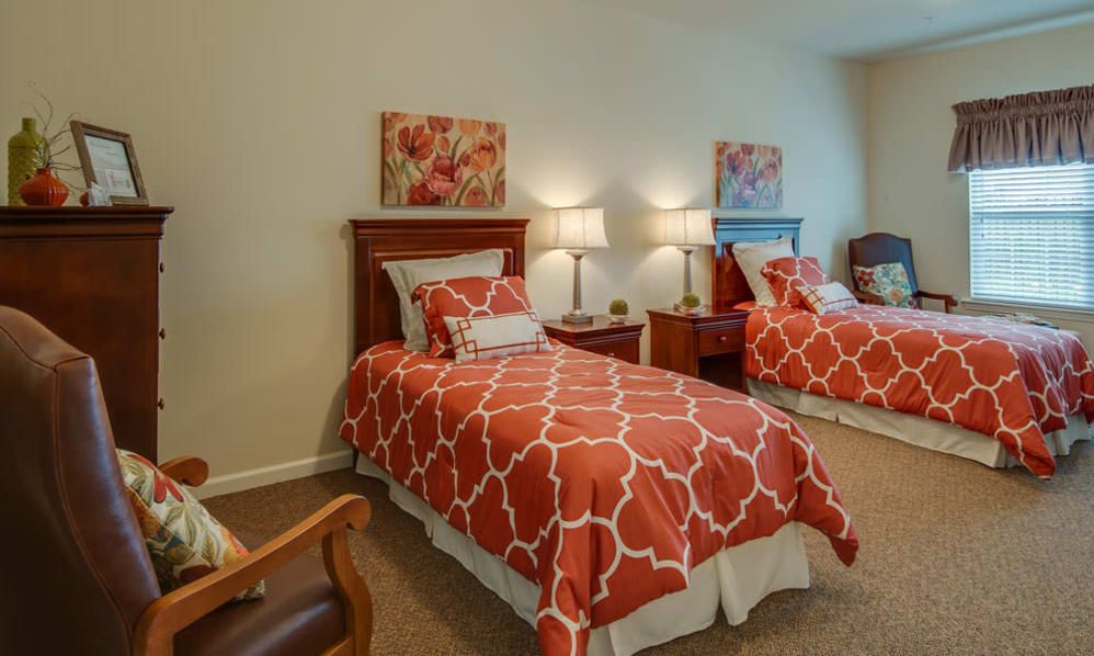 A cozy bedroom with two twin beds featuring red patterned bedding, complemented by bedside lamps and wall art.
