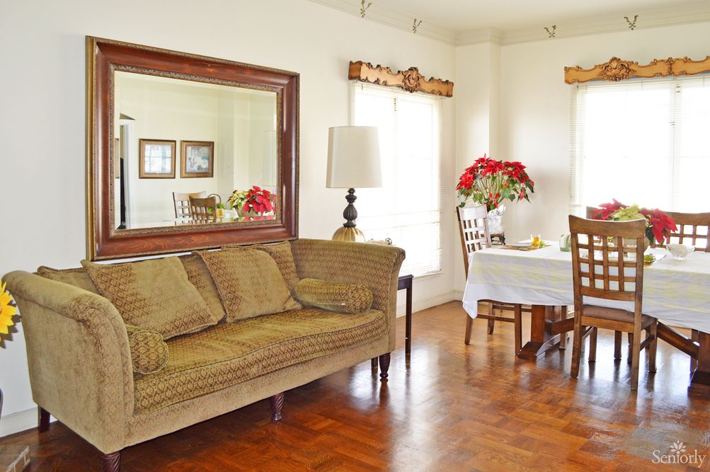 A cozy living and dining area featuring a large mirror, comfortable sofa, dining table with chairs, and floral decorations.