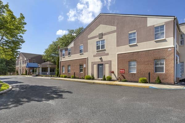 An exterior view of a building with an entrance and a parking lot under a partly cloudy sky.