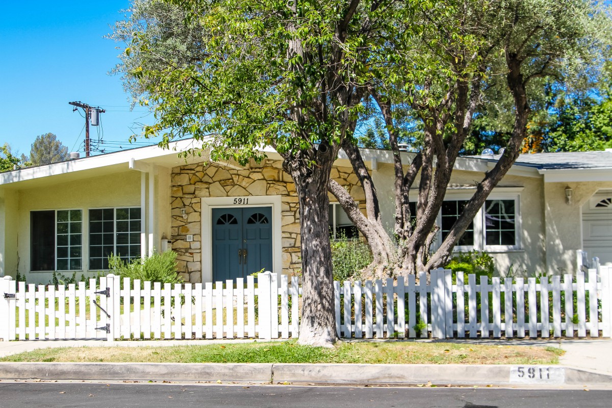 A charming house with a stone facade and white picket fence surrounded by lush greenery.