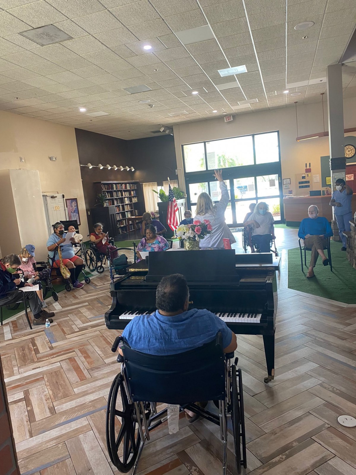 A musician in a wheelchair plays the piano for an audience in an indoor setting.