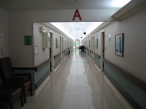 A quiet corridor in a hospital, featuring patient rooms and bright overhead lighting.
