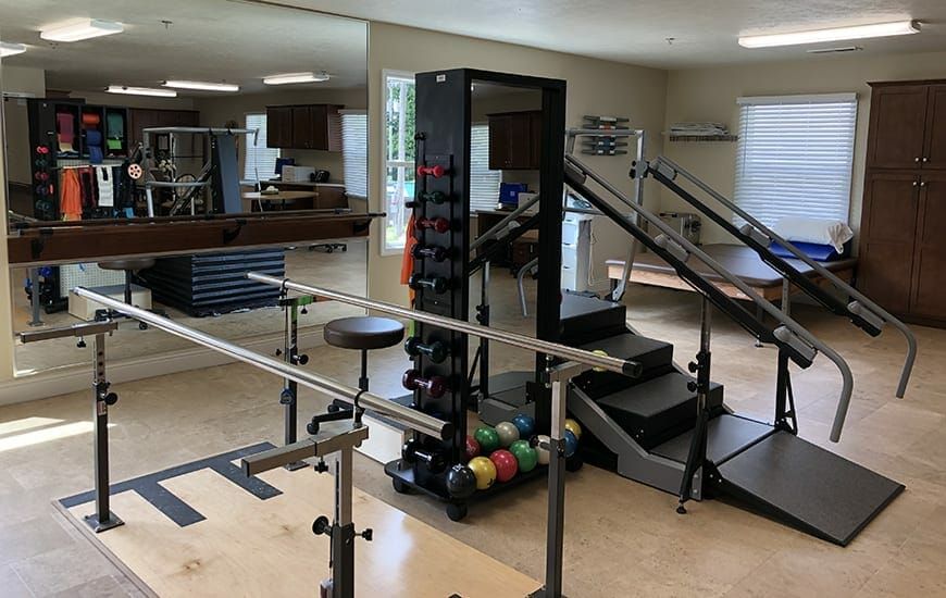 A rehabilitation gym featuring various exercise equipment, including parallel bars and weights.