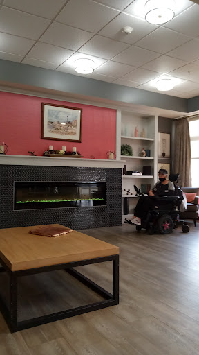 A cozy living room featuring a modern fireplace, comfortable furniture, and a person in a wheelchair enjoying the space.