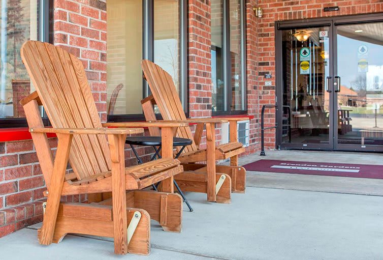 Wooden chairs on a porch in front of a brick building entrance.