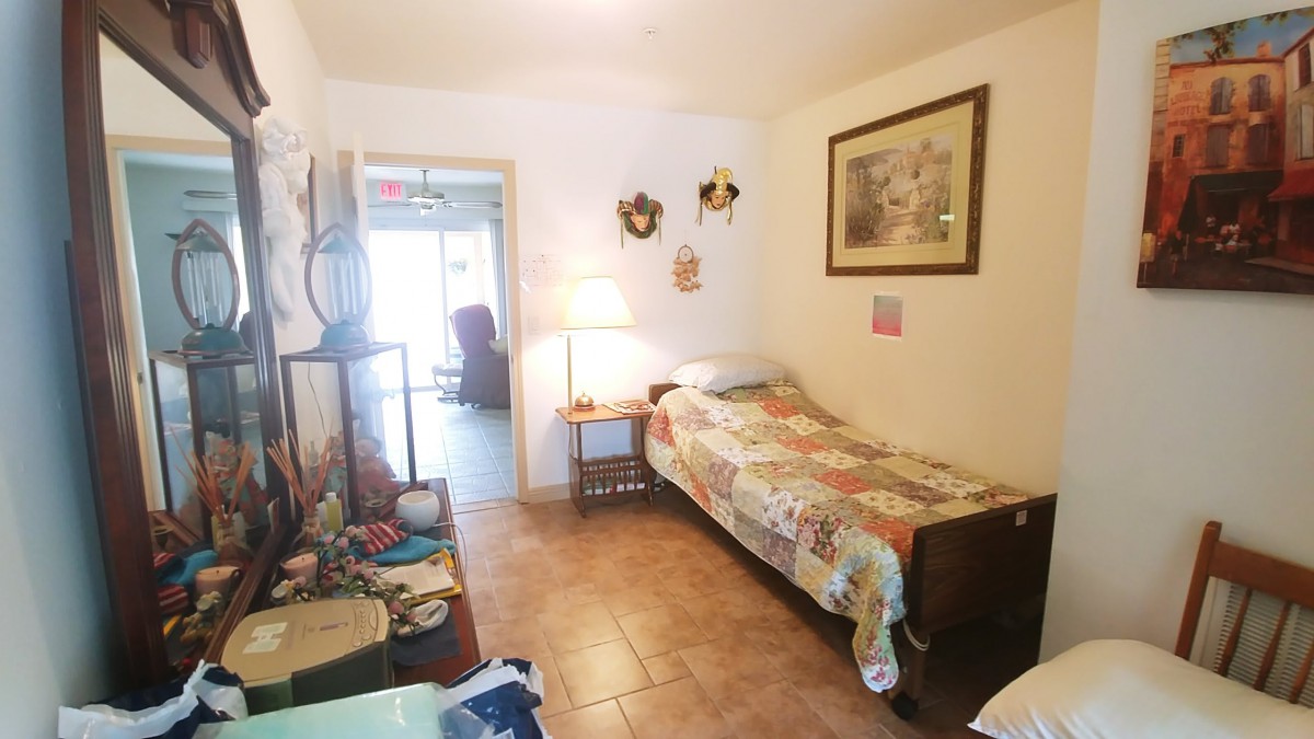 A small, cozy bedroom with a single bed, decorative items on the wall, and a lamp beside the bed.