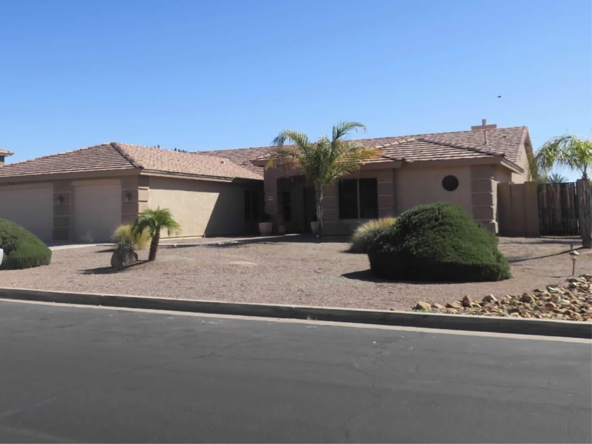 A single-story house in a suburban neighborhood with a desert landscape and palm trees.