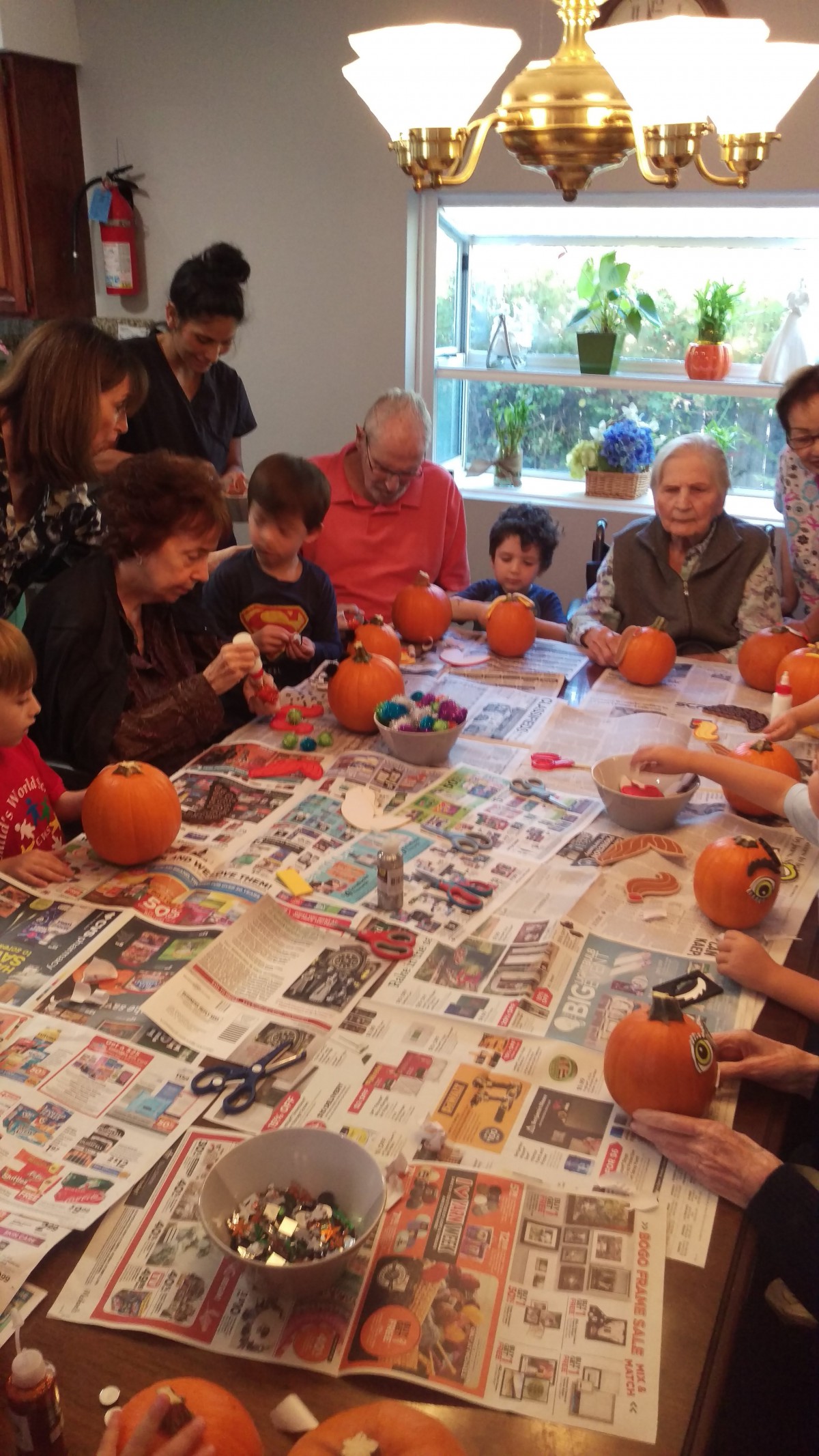 A group of adults and children gathered around a table carving pumpkins together indoors.