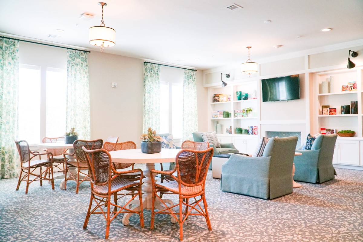 A cozy living room with a dining table, chairs, couch, and shelves, decorated in a light and airy style.