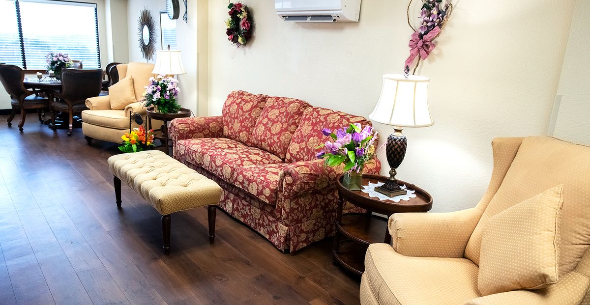 A cozy living room setup with a floral patterned sofa, side table, lamp, and decorative flowers.