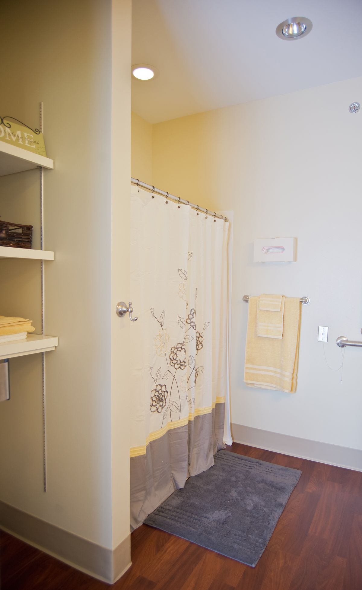 A neatly organized bathroom with a floral shower curtain, towels hung on the wall, and shelves with folded linens.