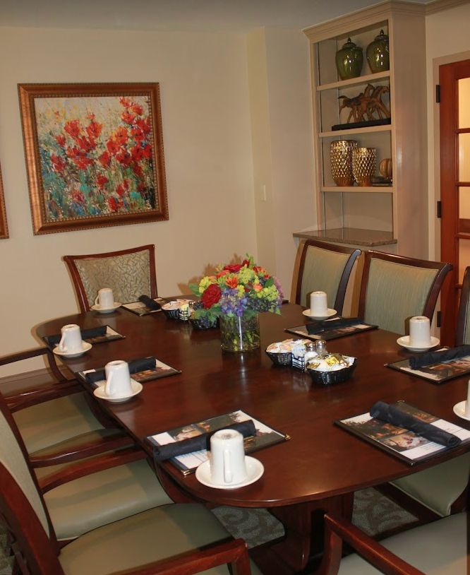 A dining room table elegantly set with cups and a floral centerpiece, surrounded by chairs and decorated with artwork.