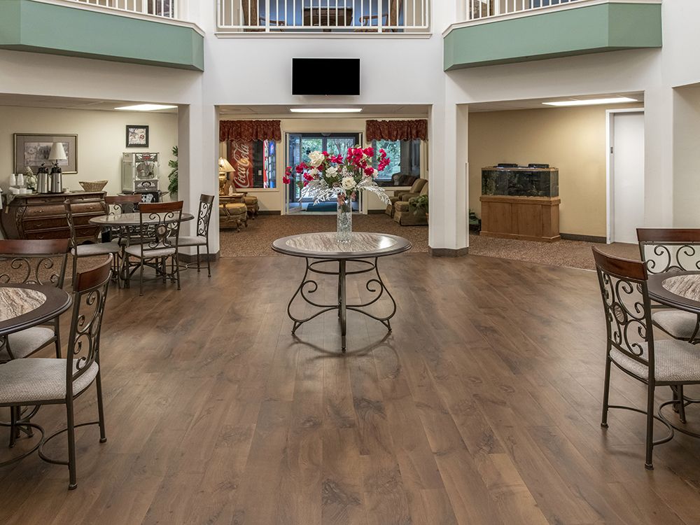 A spacious and modern lobby with wooden flooring, featuring tables, chairs, and a decorative centerpiece.