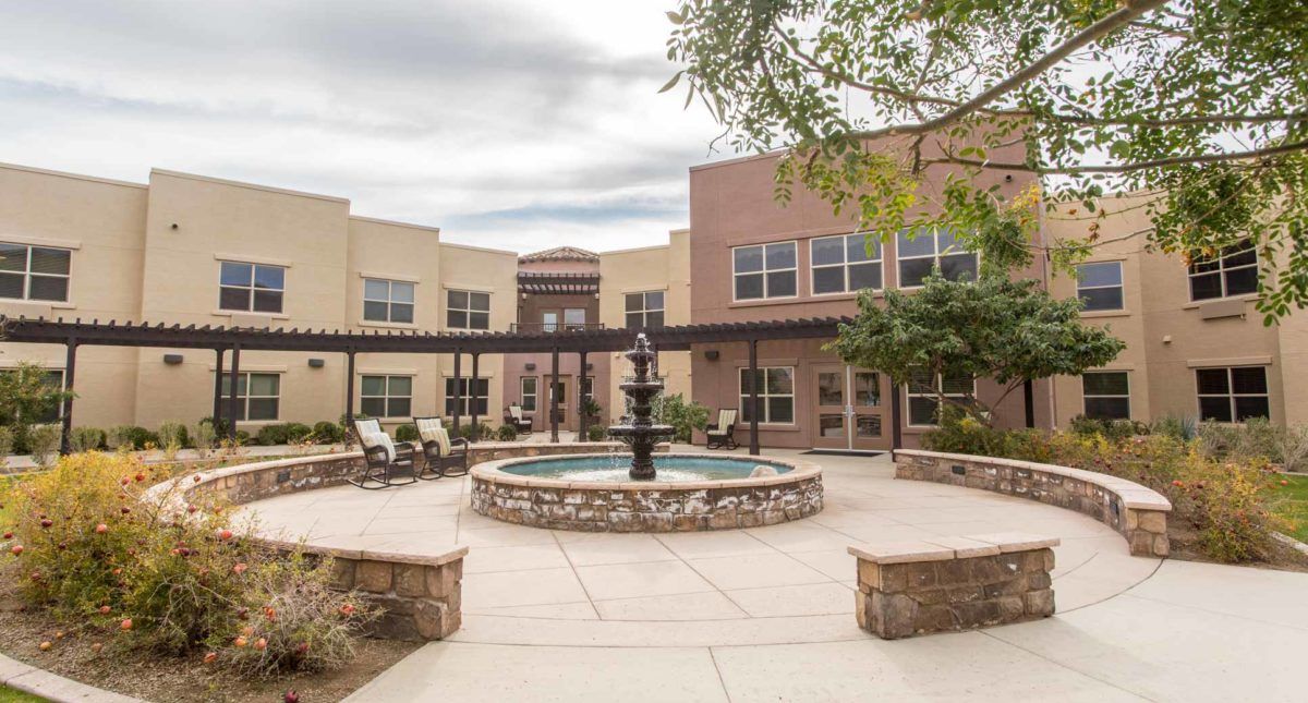 A peaceful courtyard featuring a central fountain, surrounded by a beige and brick building with outdoor seating areas.