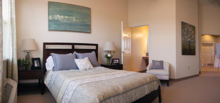 A cozy bedroom with a neatly made bed, bedside lamp, and wall artwork.