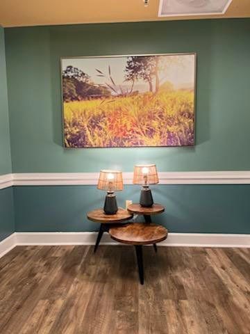 A cozy corner with vibrant wall art and stylish table lamps on a wooden table, surrounded by teal walls and hardwood flooring.