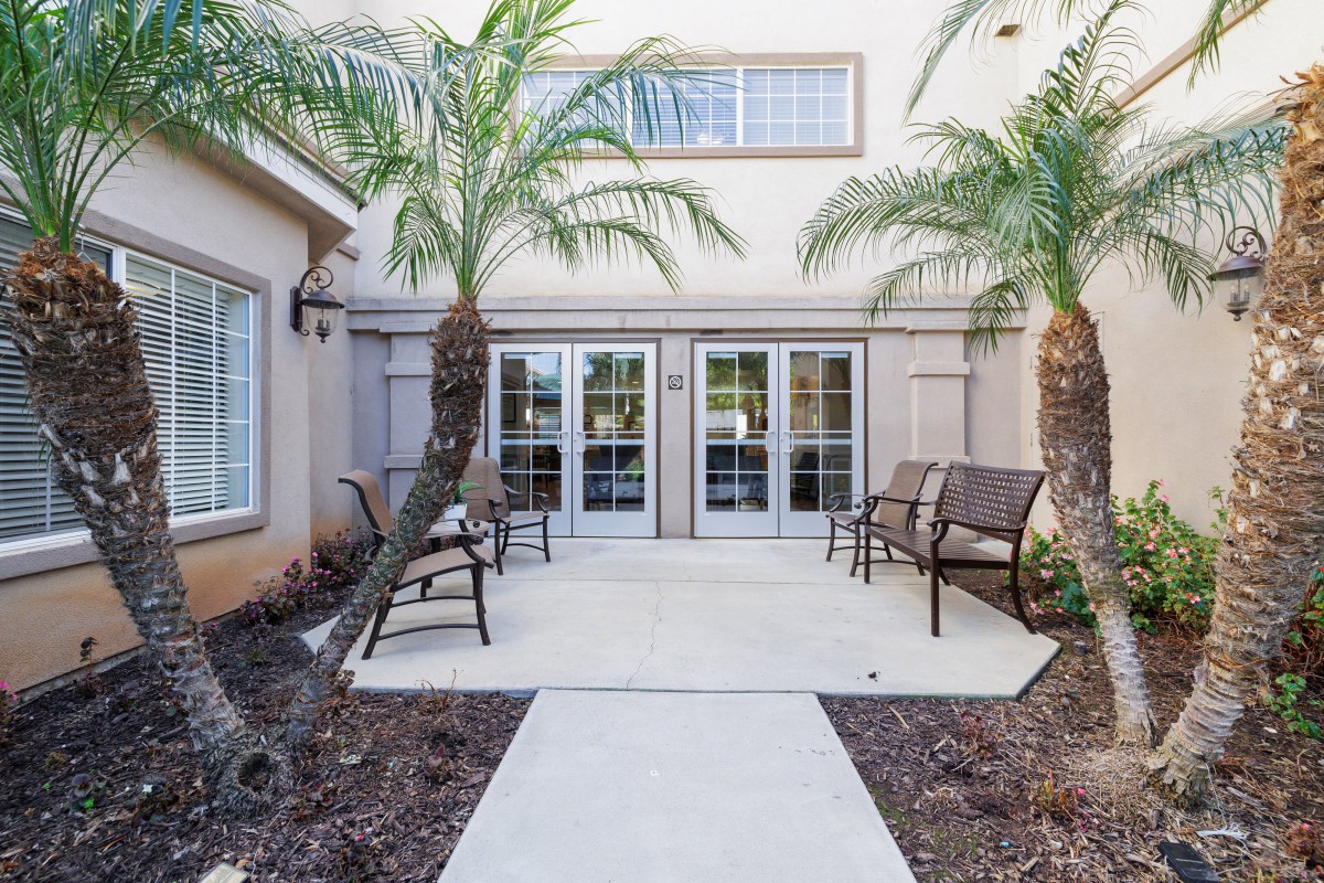 A cozy patio area with benches and palm trees outside a building.