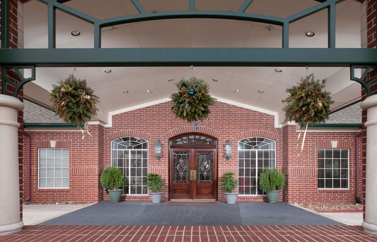 A welcoming building entrance adorned with wreaths and potted plants.