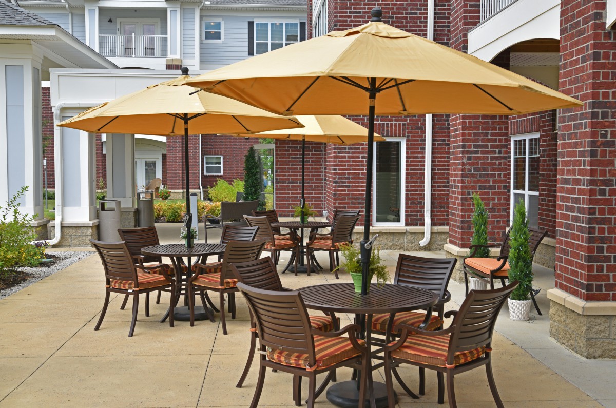 An outdoor patio area with tables, chairs, and umbrellas near a brick building.