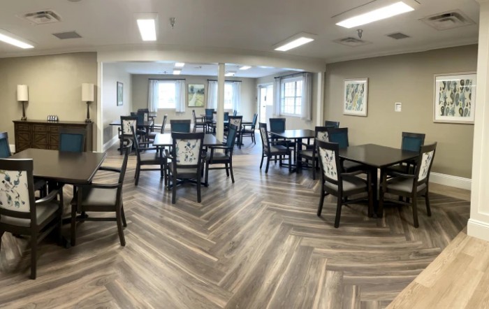 An empty dining room with neatly arranged tables and chairs, illuminated by overhead lights.