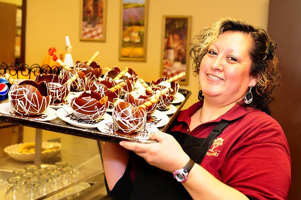 A woman smiling while holding a tray of decorated desserts.