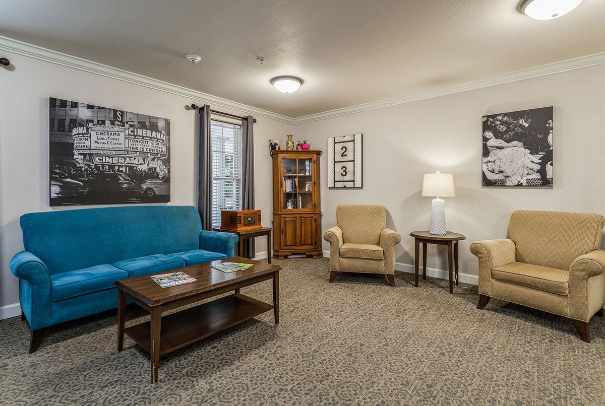 A cozy living room with a blue sofa, two beige armchairs, a wooden coffee table, and decorative artwork on the walls.