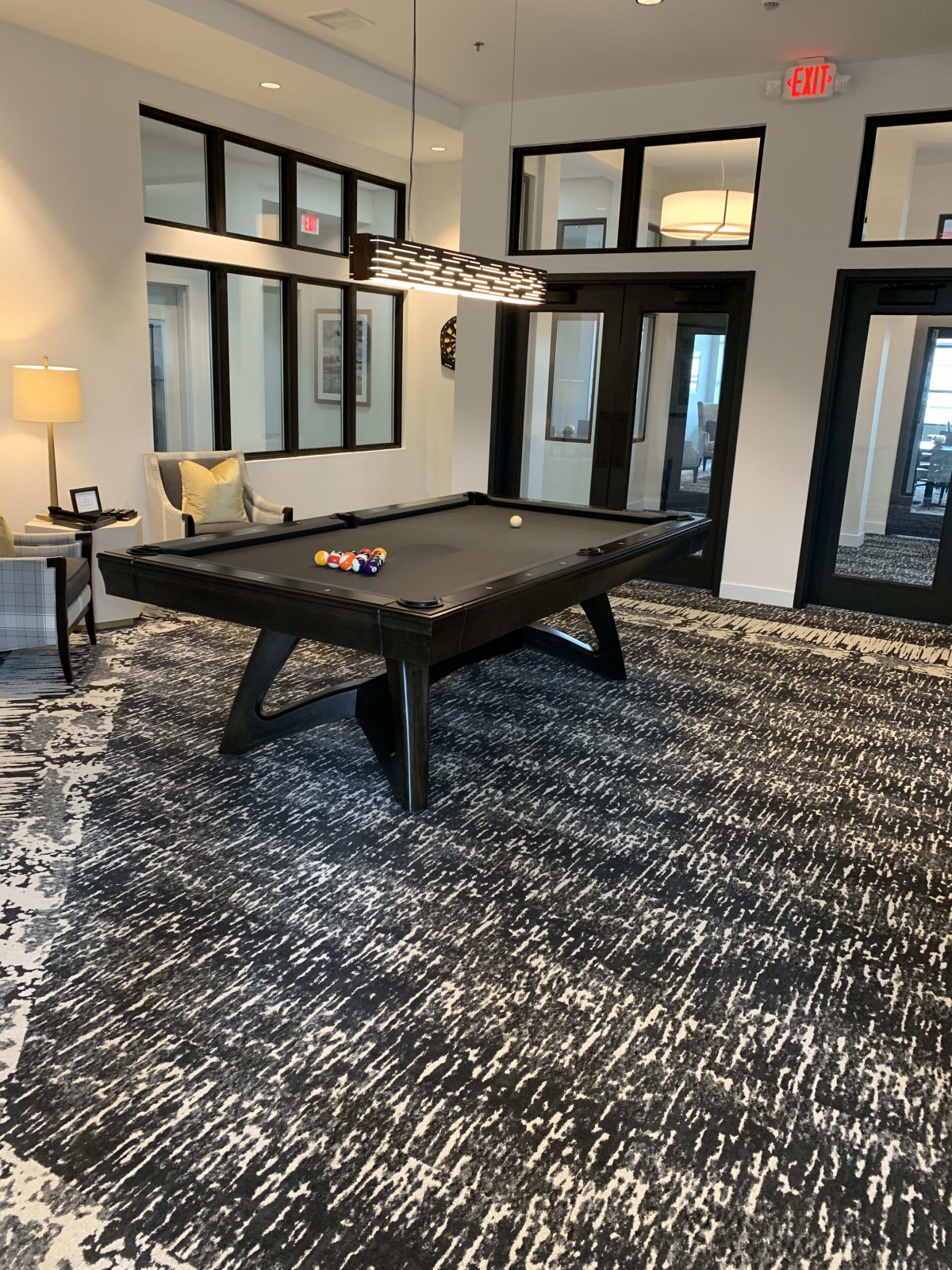 A modern recreation room featuring a stylish pool table, contemporary carpet, and large windows.