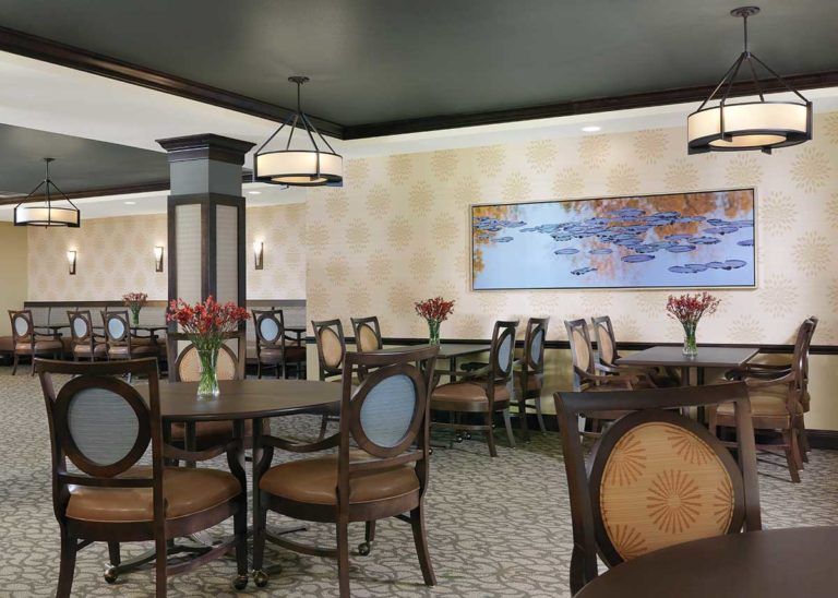 A well-decorated restaurant dining area with arranged tables and chairs, illuminated by elegant lighting fixtures and adorned with floral centerpieces and wall art.